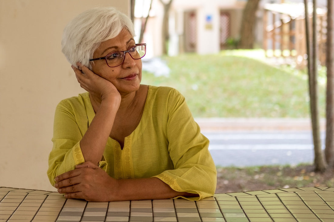 An older woman rests her head on her hand and stares into the distance