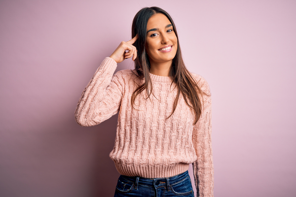 woman in a pink sweater pointing to her brown hair
