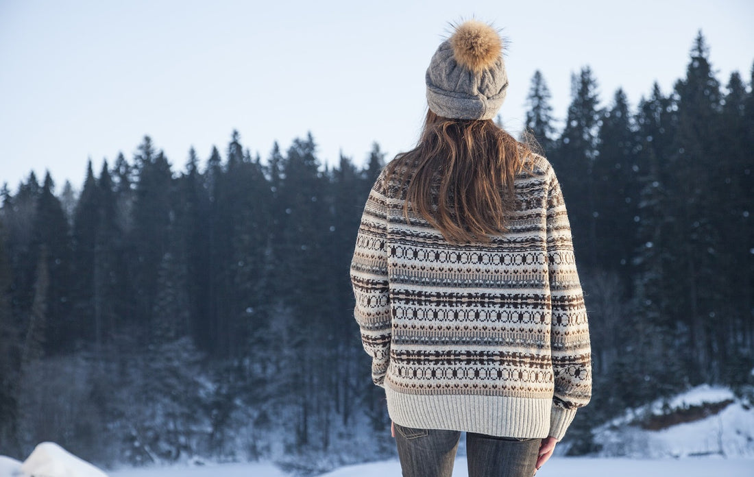 A woman looks out into a snowy field in a sweater and hat