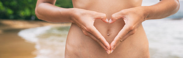 Young woman signs a heart over her stomach because she knows the underlying causes of SIBO and could end its symptoms.