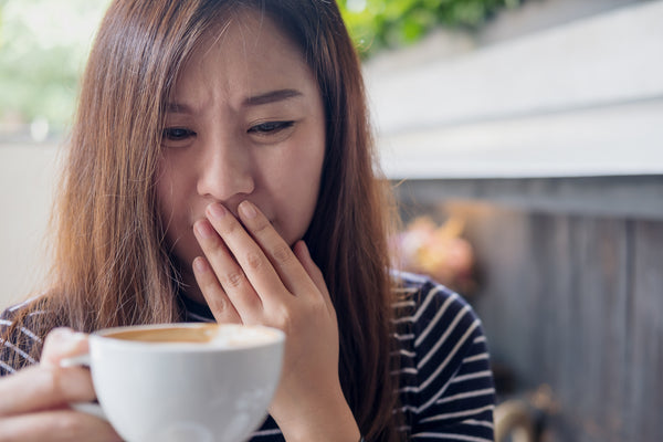 woman holding her mouth as she looks at coffee