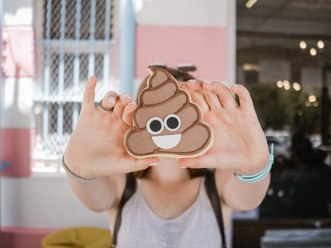 A woman holds a cookie with the poop emoji on it
