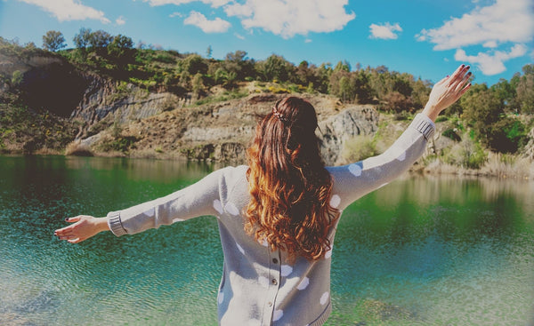 A happy woman spreads her arms in front of a lake and hill