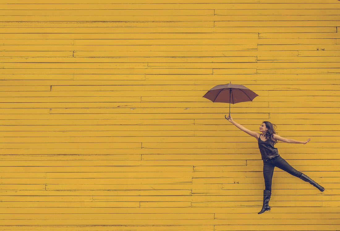 a woman floating with an umbrella on a yellow background 